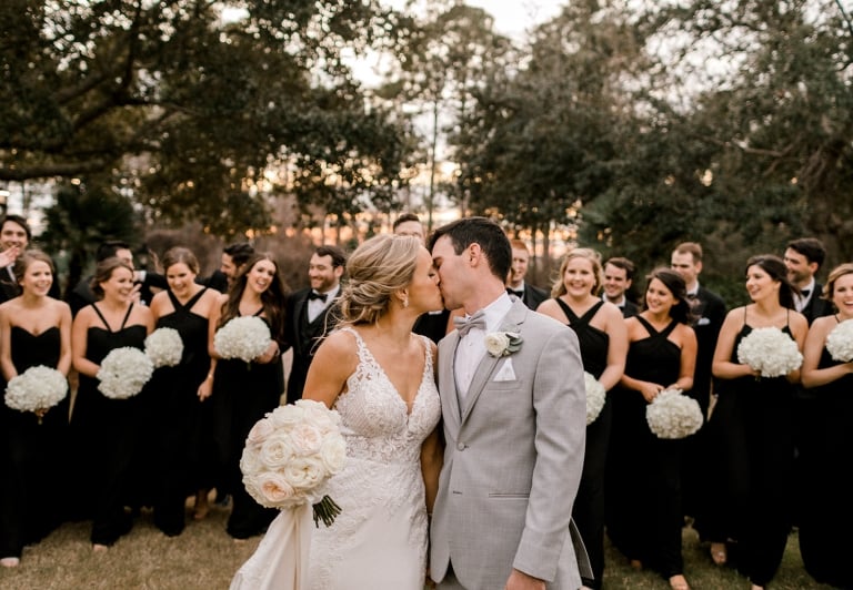 Bride and groom kissing with wedding party standing behind them
