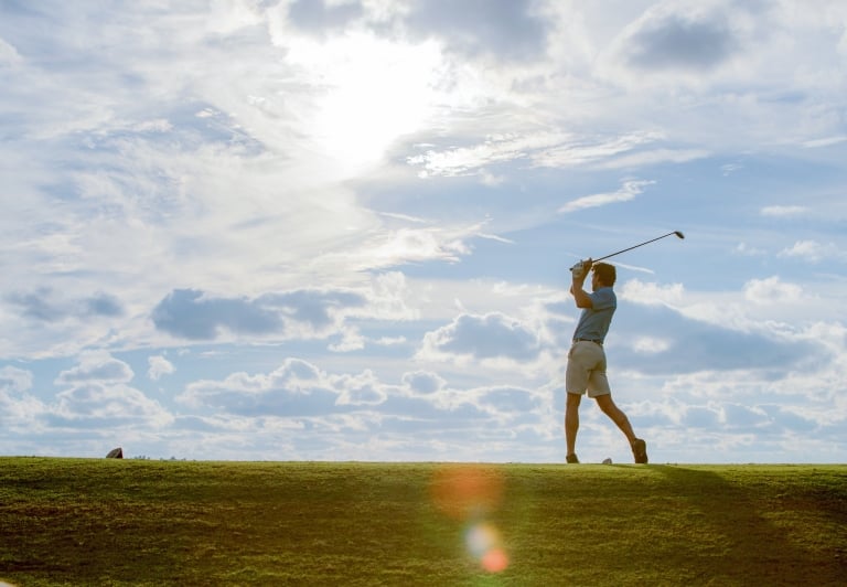 man playing golf with a blue sky in the background