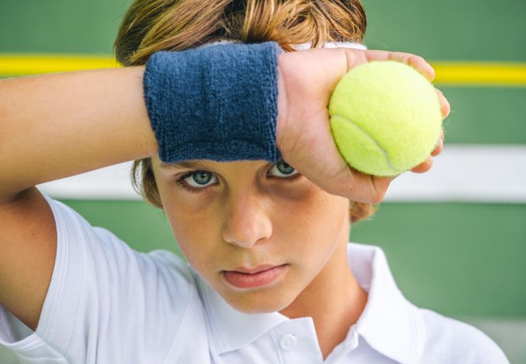 kid wiping his brow playing tennis