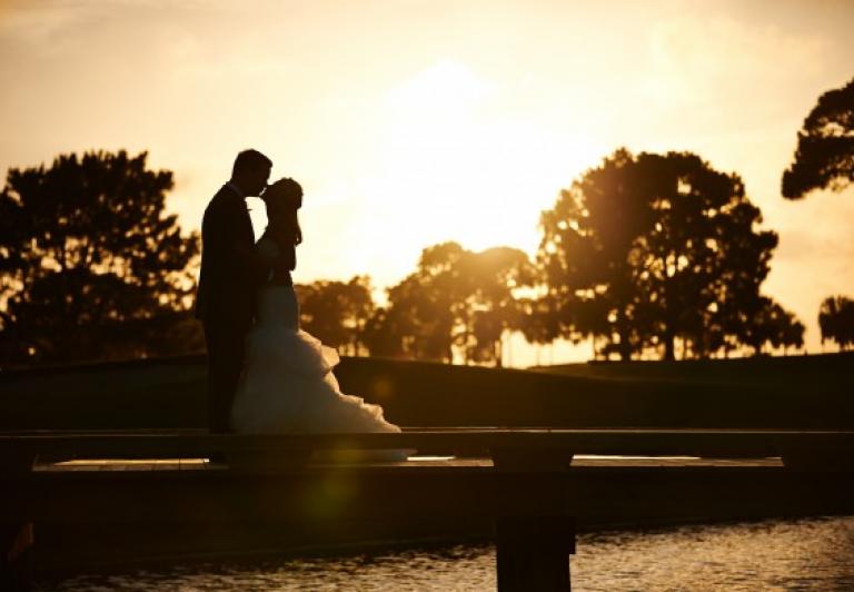 Bride and groom kissing on golf course at sunset