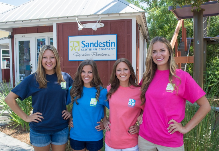 Four women posing outside of the Sandestin Clothing Company store with branded shirts