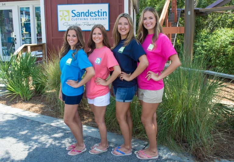 Four women posing outside of the Sandestin Clothing Company store with branded shirts