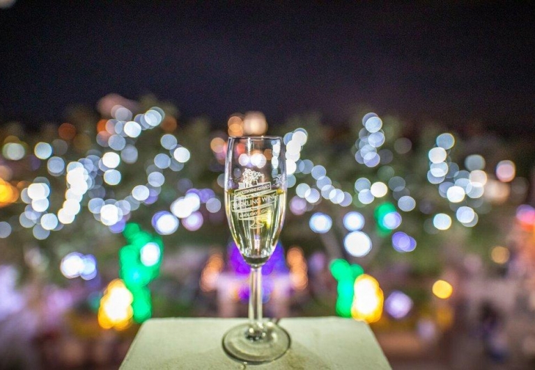 A glass of sparkling wine on a patio with bright lights in the background