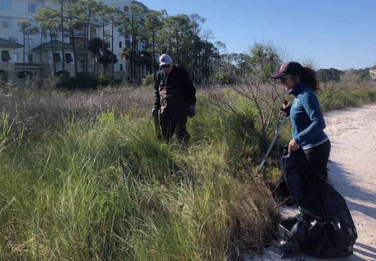 two people collecting trash in marsh