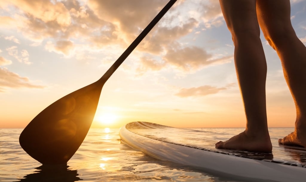 an individual paddleboarding at sunset