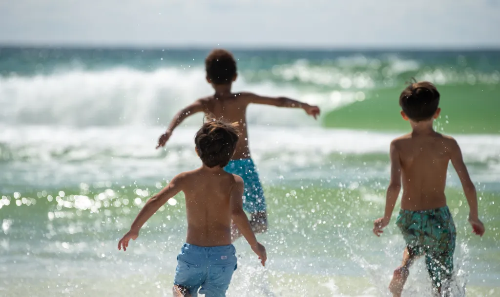 Three children running from the beach towards the blue ocean