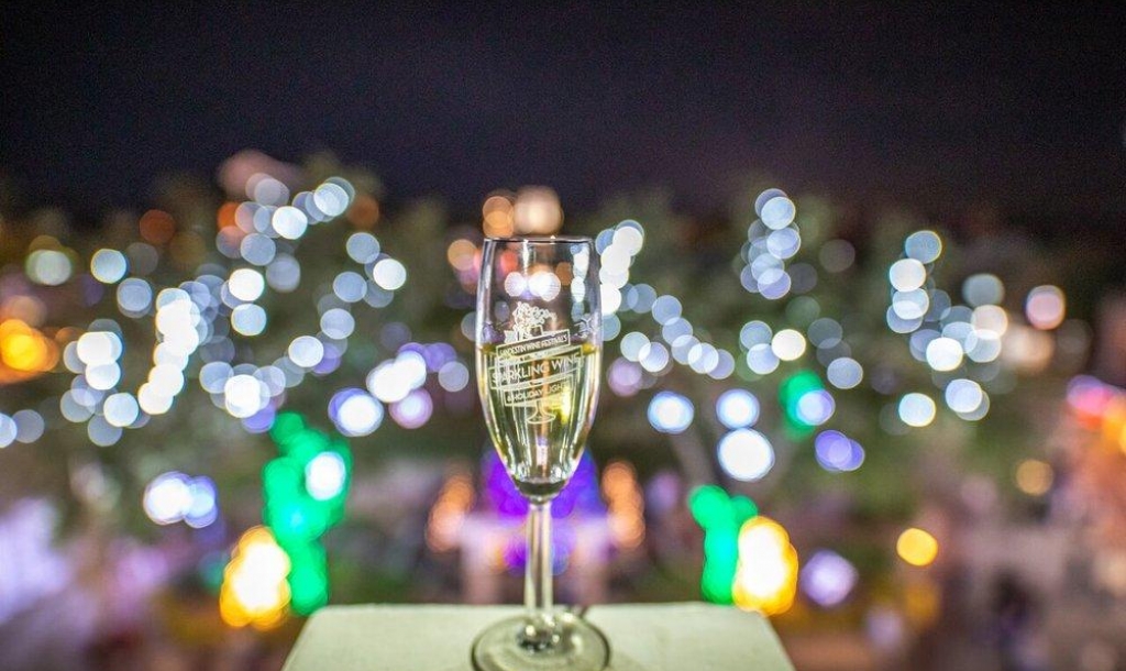 A glass of sparkling wine on a patio with bright lights in the background