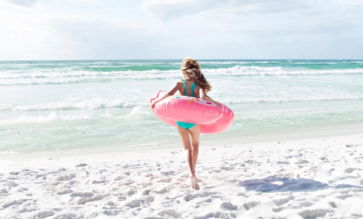 Child running towards the ocean carrying an inflatable donut 