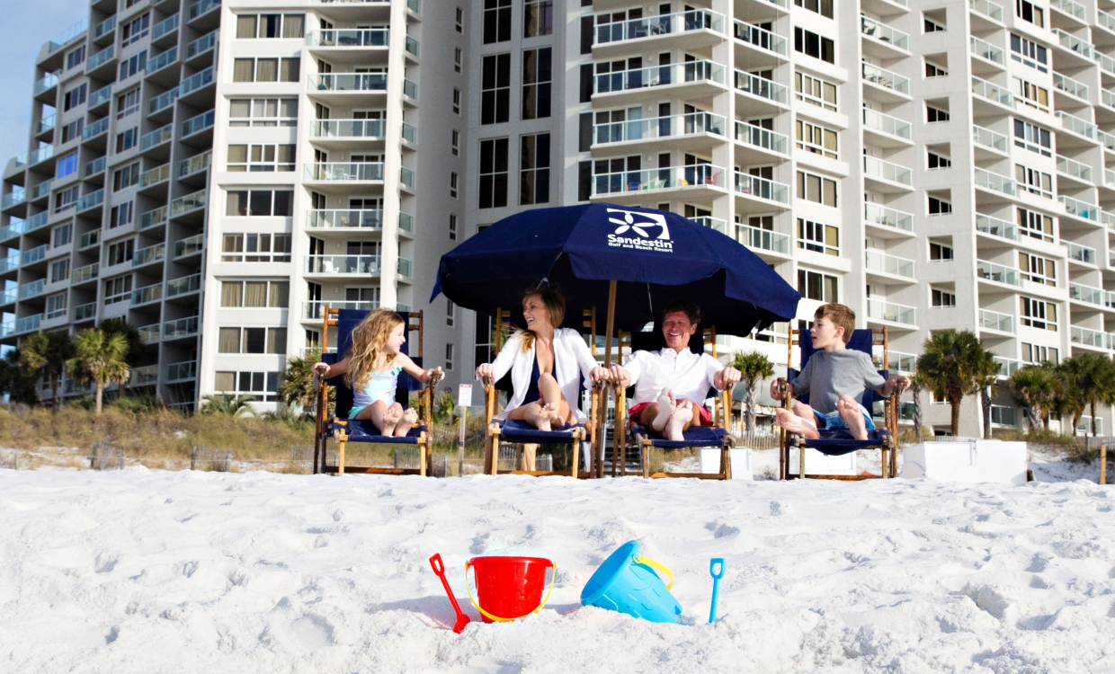 family sitting on the beach under an umbrella with sand buckets in the foreground
